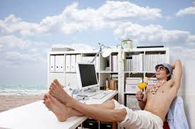 Man at the beach sits with his feet up on an office desk with white filing cabinets in the background as he sips on a cocktail and relaxes